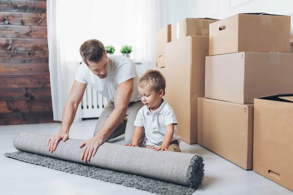 Father and Young Son Rolling Up Carpet With Moving Boxes Behind Them - Tupelo Mover - House To House Moving LLC