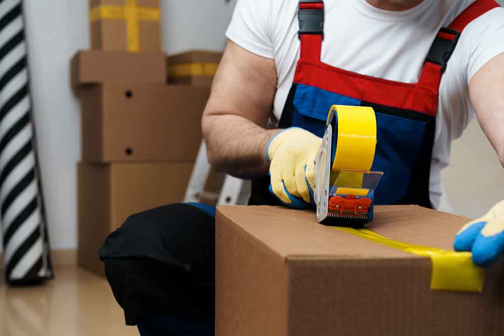 Male Mover Taping Packed Box WIth Yellow Duct Tape - Packing and Unpacking Services by House to House Professional Movers In Tupelo, Mississippi